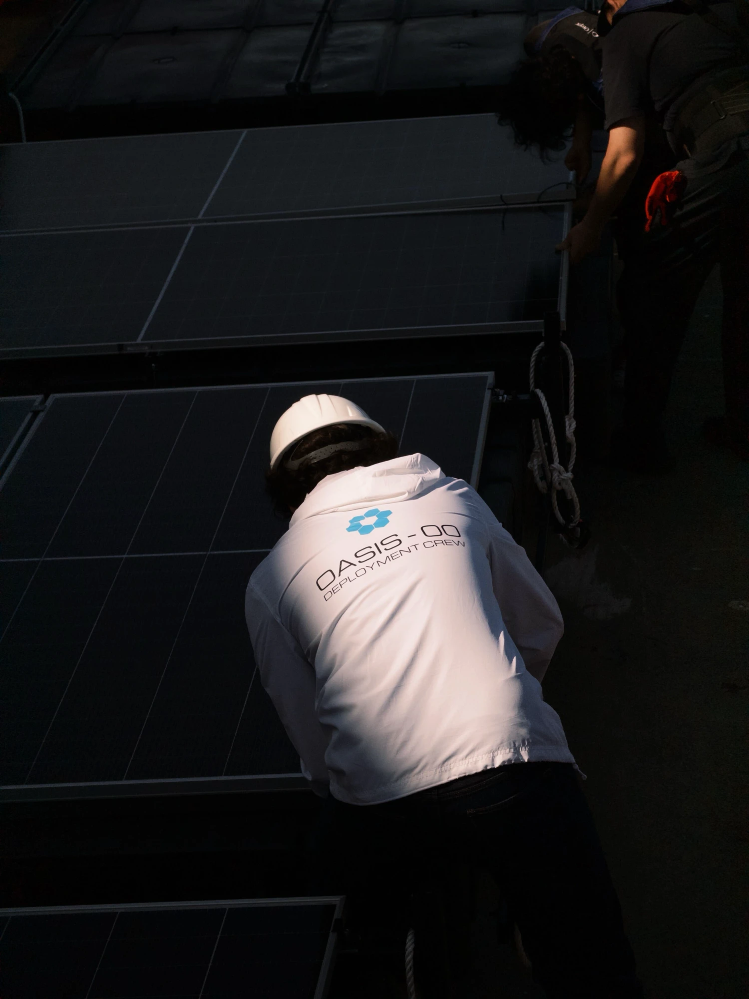 a crew member in an OASIS-00 deployment crew jacket fitting a solar panel